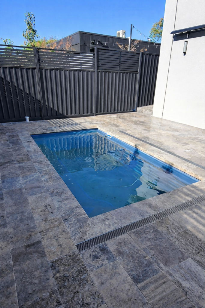 Wetlay travertine poolside paving installation including stainless steel drainage alongside pool to assist with water management 